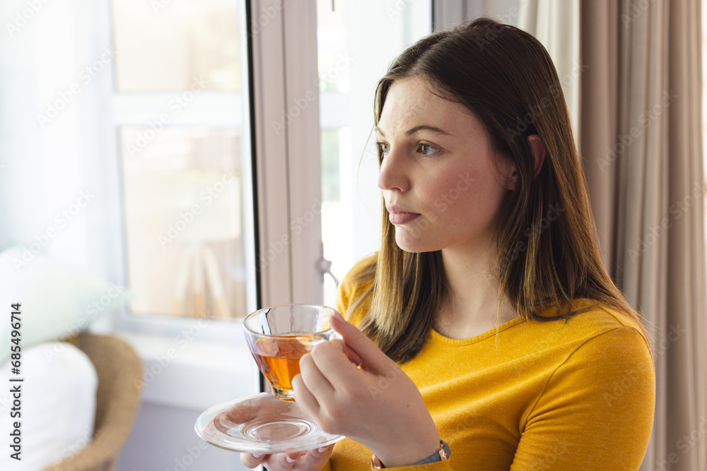 Portrait of thoughtful caucasian woman holding tea cup by window in living room at home, copy space Portrait of thoughtful caucasian woman holding tea cup by window in living room at home, copy space