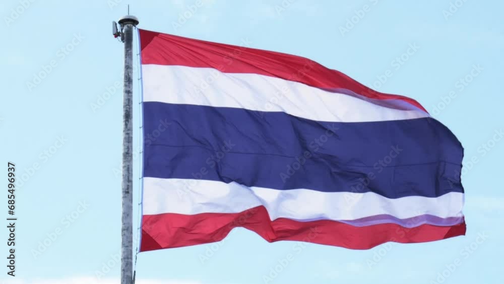 Thailand national flag hoisted on a white tall steel pole blown by the wind creating an animated wave on a backdrop of a clear blue sky and white clouds. Thailand national flag hoisted on a white tall steel pole blown by the wind creating an animated wave on a backdrop of a clear blue sky and white clouds.