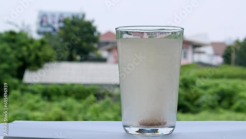 A glass filled with water on the window sill is bubbling with a tablet of sodium bicarbonate antacid inside the bottom of the glass. photo