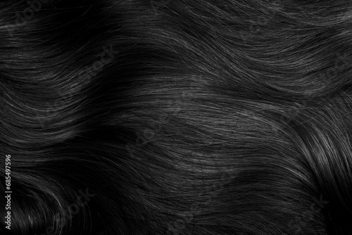 Brunette or black hair. Female long dark hair in black. Beautifully laid curls. Closeup texture in a dark key. Hairdressing, hair care and coloring. Shading gray hair. Background with copy space.
