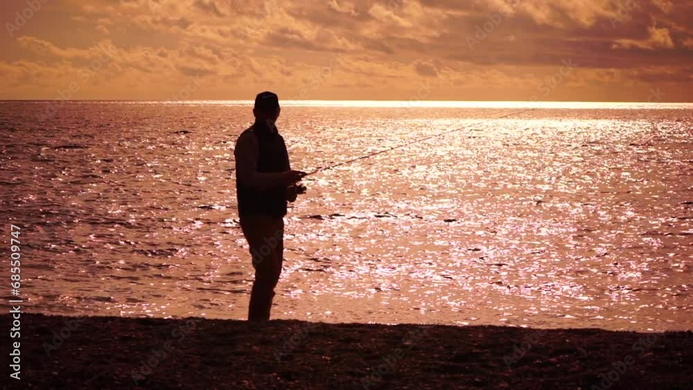 man standing on pier, holding a fishing rod and preparing to cast it into sea ocean at warm sunset. Man hobby fishing on sea tightens a fishing line reel of fish summer. Calm surface sea. Slow motion.