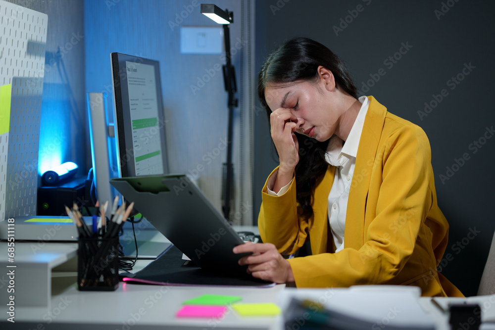 Asian businesswoman stressed while working on documents information on pc computer Feeling tired, headaches, and eye strain at work within the company.