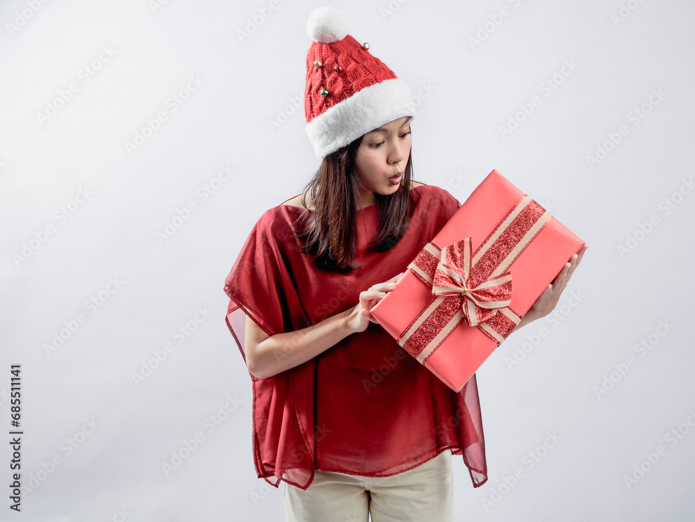 A portrait of a happy Asian woman celebrating Christmas, wearing a red dress and Santa hat, while carrying a gift box. Isolated against a white background. A portrait of a happy Asian woman celebrating Christmas, wearing a red dress and Santa hat, while carrying a gift box. Isolated against a white background.