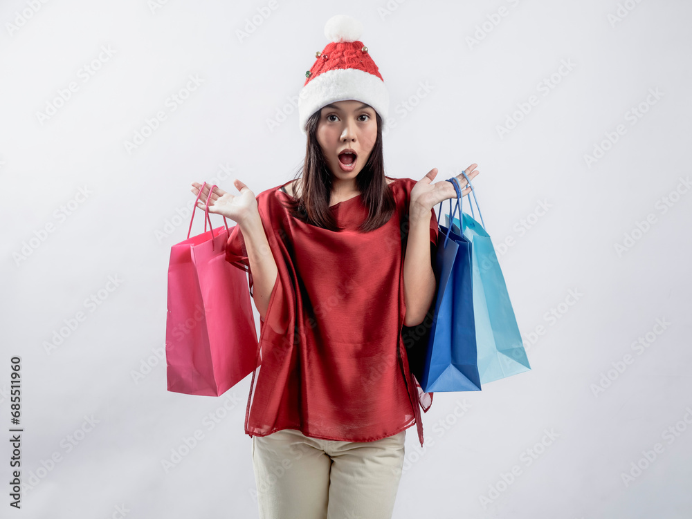 A portrait of a happy Asian woman celebrating Christmas, wearing a red dress and Santa hat, carrying a shopping bag. Isolated against a white background. A portrait of a happy Asian woman celebrating Christmas, wearing a red dress and Santa hat, carrying a shopping bag. Isolated against a white background.