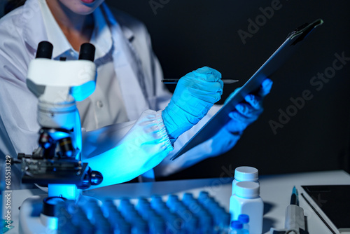 Research laboratory. Female scientist writes medical results of a document or report analyzing chemical tests with a microscope drug samples Concept of scientific research and development in biology.
