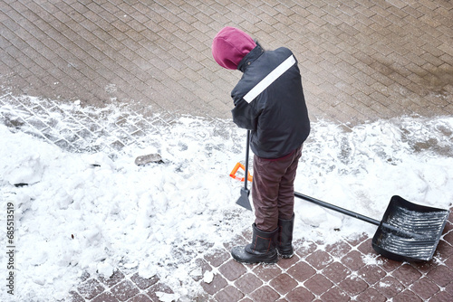 Man breaking ice with hand ice chopper, tool for break ice. Worker remove ice and snow with icebreaker from snowy sidewalk, top view. Street cleaning in winter season, cleaning road with razor scraper