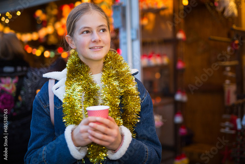 Happy teenagers girl holding hot cup of coffee in hands at street christmas fair