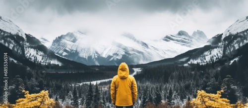 Someone in a yellow jacket admiring the snowy forest and distant mountains on a cloudy day in the Canadian Rockies.