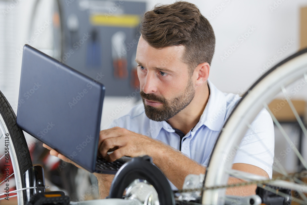 young man repairing bicycle with the help of a laptop young man repairing bicycle with the help of a laptop