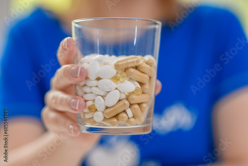 Kobieta trzyma szklankę wypełnioną lekami zamiast wody