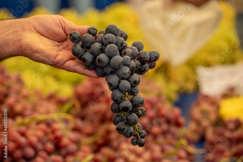 A bunch of grapes in the hands of the seller in the market. Close-up of carefully selected ripe grapes. Red wine grapes. Healthy organic sweet fruit. Vitamin diet for women