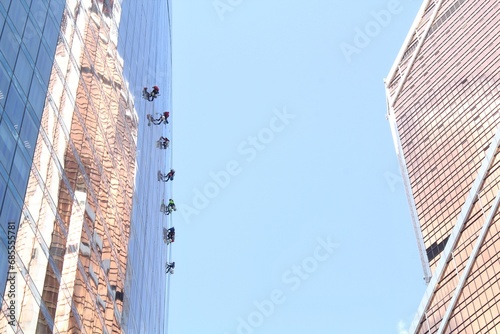 Team of professional climber workers cleaning outdoor windows of residential skyscraper. Industrial alpinism mountaineers washing outside at heights the glass facade of modern office building.
