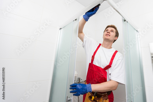 Young man repairing door of shower cabin in bathroom.