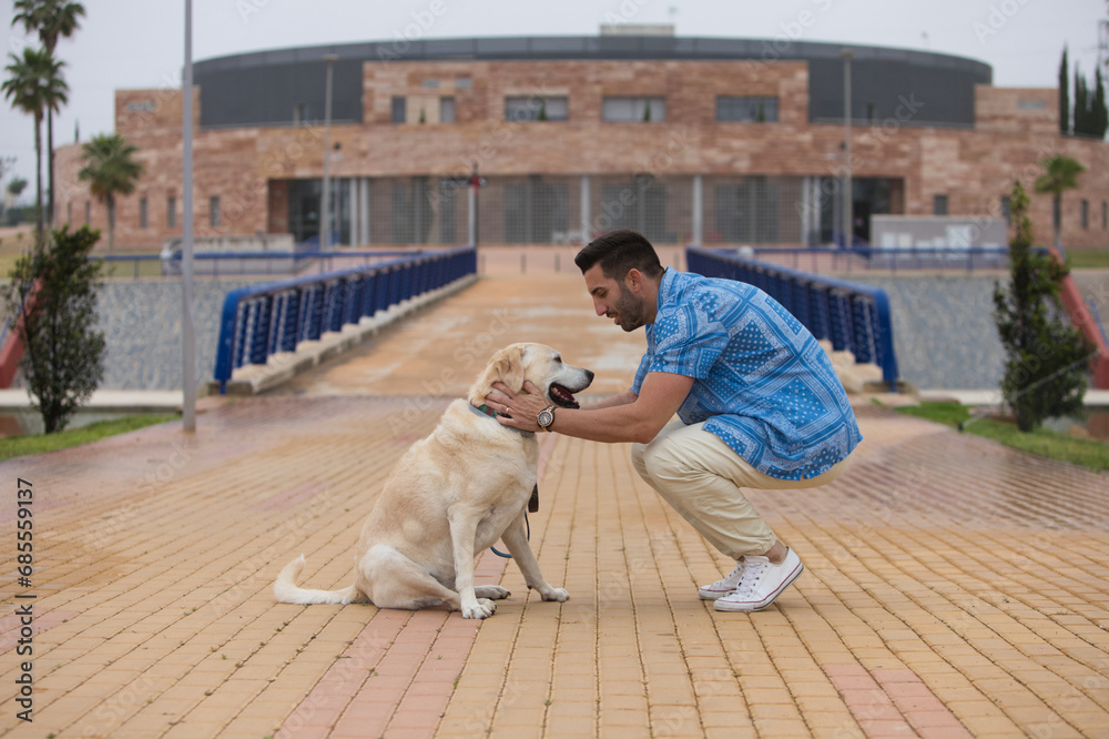 Handsome young man with beard and his Labrador retriever dog stop for a rest. The man looks at the dog with affection and love and they bring their faces close together. International dog day. Handsome young man with beard and his Labrador retriever dog stop for a rest. The man looks at the dog with affection and love and they bring their faces close together. International dog day.
