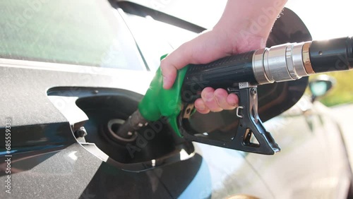 Fuel nozzle in the tank of a car at a gas station. Concept of the cost of gasoline per liter. Gasoline quality, car fuel consumption. A handgun against the backdrop of the sun. Slow motion photo