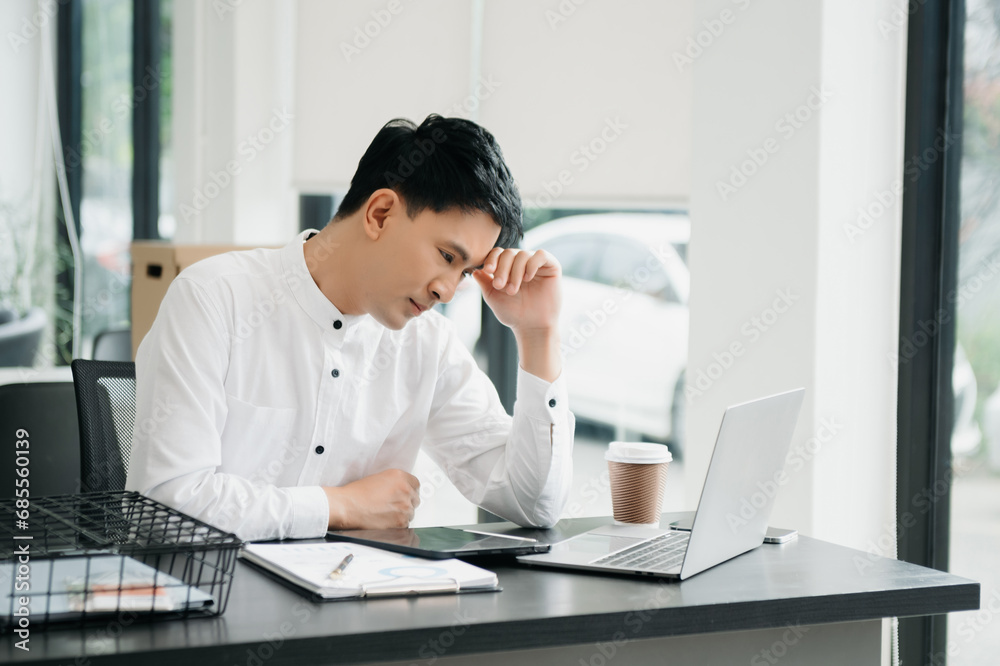Frustrated young businessman working on a laptop computer sitting at his working place Frustrated young businessman working on a laptop computer sitting at his working place