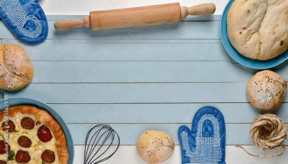 Old turquoise wooden kneading board framed with loaves of bread, pizza, potholders and rolling pin. Top down view. Flat lay image background.