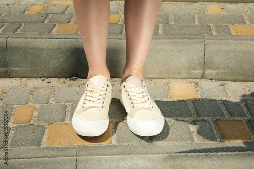 Stylish white sneakers on women's legs on cobblestones