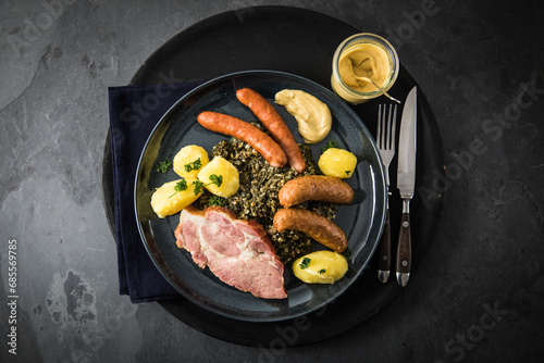 Oldenburger Grünkohl mit geräucherter Kohlwurst, Pinkel, Kassler Nacken, Kartoffeln, Senf, Petersilie auf Teller und dunkel schwarz Schiefer Hintergrund