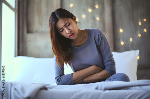 Young woman suffering from a stomachache on the bed at home, concept of food poisoning. Female holding her stomach with a pained expression, stomach disease © Sippung