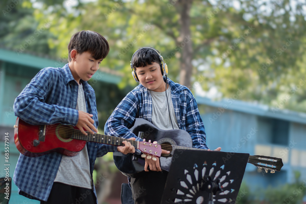 Fototapeta premium Asian cute boys doing summer activity at their front yard by playing and showing acoustic guitars, freestyle of children life concept.