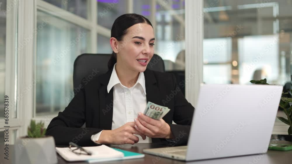 Optimistic manager using digital laptop for talking on video call while holding dollar banknotes in hands. Professional lady conducting online interview and showing possible salary in office. Optimistic manager using digital laptop for talking on video call while holding dollar banknotes in hands. Professional lady conducting online interview and showing possible salary in office.