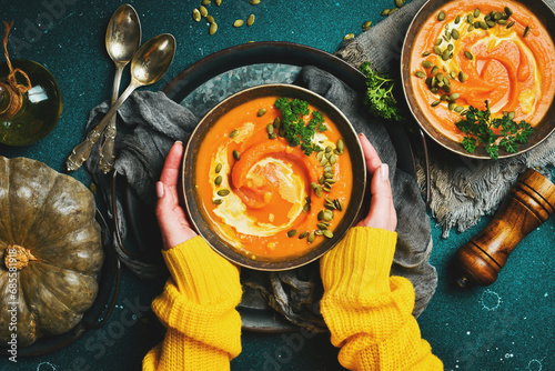 Female hands holding a bowl of pumpkin cream soup on a dark background. Autumn food concept. Top view. photo