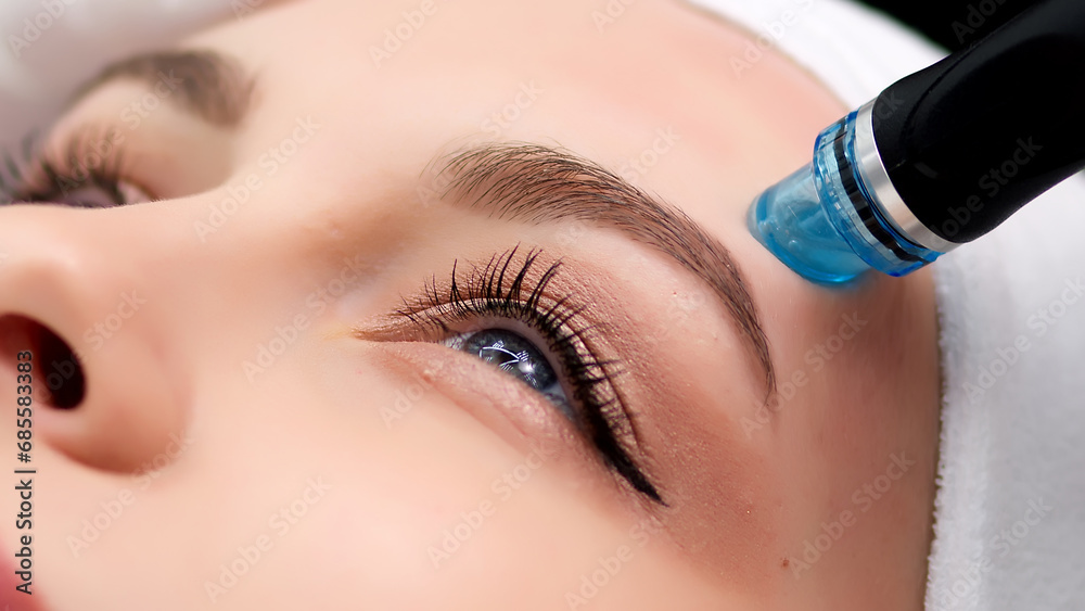 Professional dermatologist in medical gloves doing hydro peeling procedure for beautiful woman patient in cosmetology clinic. Close up facial treatment.