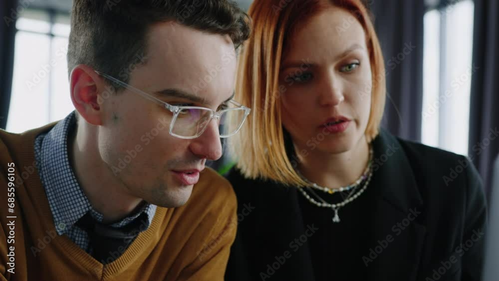 Portrait of two colleagues who are sitting in a meeting room and looking at a laptop screen. A team of millennials in the office Portrait of two colleagues who are sitting in a meeting room and looking at a laptop screen. A team of millennials in the office