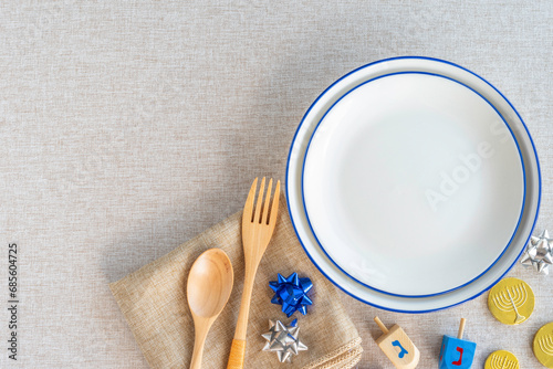 Hanukkah table setting with plates, wooden cutlery, traditional decorations on cotton fabric background. Hebrew letters on dreidels say: 