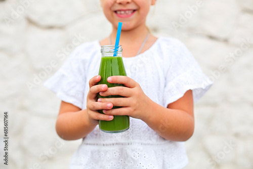 Little girl is drinking green fresh juice using straw outdoors