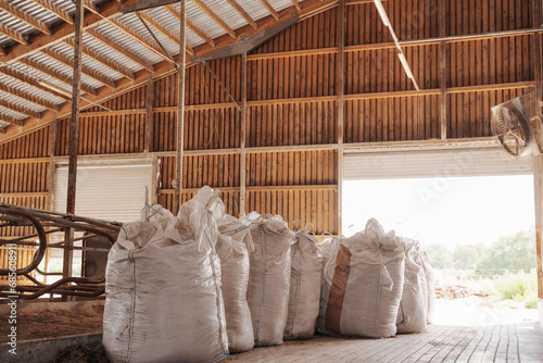 A row of large, filled industrial feed bags neatly aligned inside a rustic farm storage barn