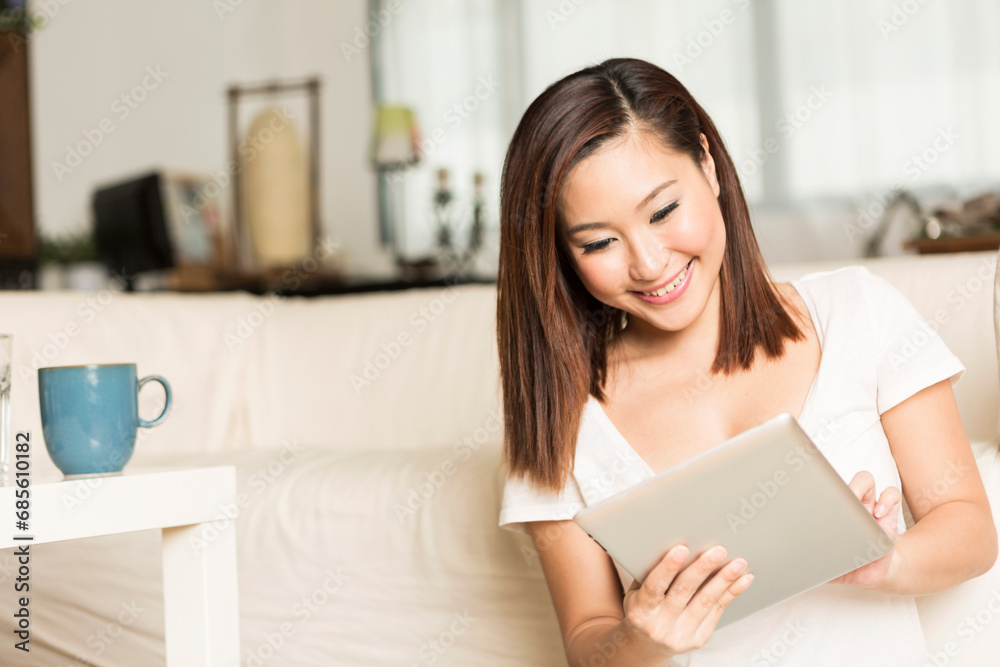 Chinese woman sitting on sofa using Digital Tablet Chinese woman sitting on sofa using Digital Tablet