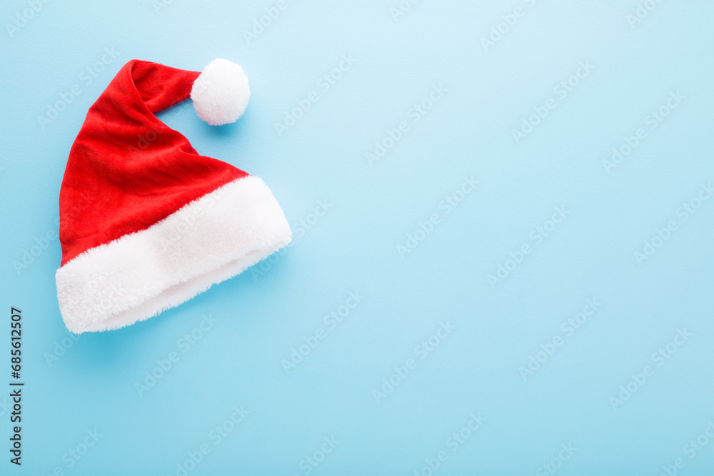 Bright red hat with white fur on light blue table background. Pastel color. Closeup. Garment for Christmas celebration. Empty place for text, quote or sayings. Top down view. Bright red hat with white fur on light blue table background. Pastel color. Closeup. Garment for Christmas celebration. Empty place for text, quote or sayings. Top down view.