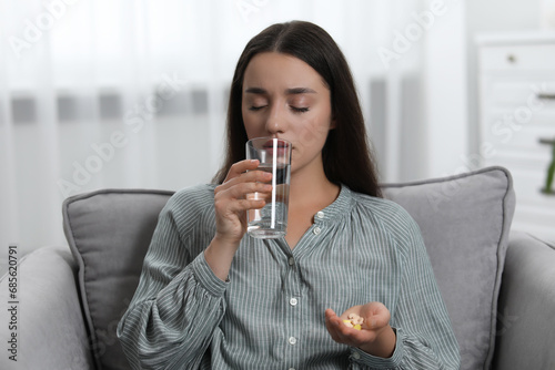 фотографія Depressed woman with glass of water taking antidepressant pills in armchair indo