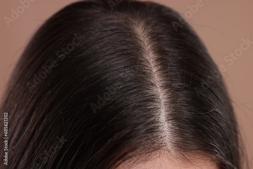 Woman with healthy dark hair on beige background, closeup