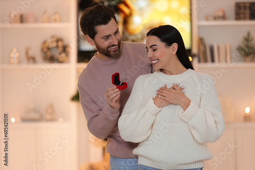 Making proposal. Man with engagement ring surprising his girlfriend at home on Christmas photo