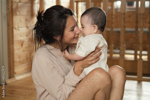 Natural Connection: A content mom and her giggling baby bask in the glow of unconditional love, framed by the warm wooden walls and a sunlit window photo