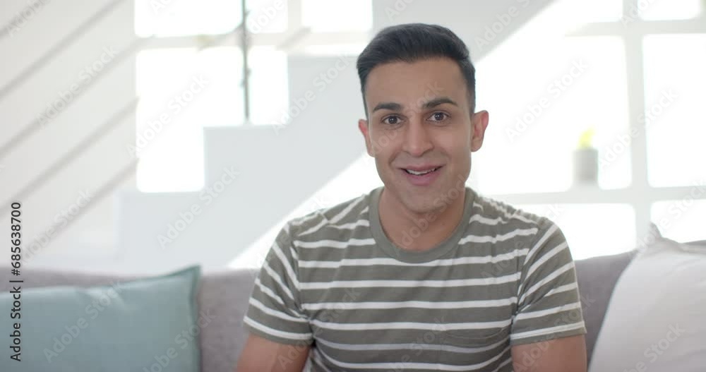 Happy surprised biracial man having video call and opening present in sunny living room, slow motion Happy surprised biracial man having video call and opening present in sunny living room, slow motion