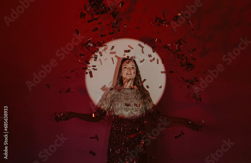 Young woman catching confetti in spotlight against red background photo