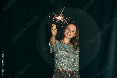 Woman holding sparkler in front of black curtain photo
