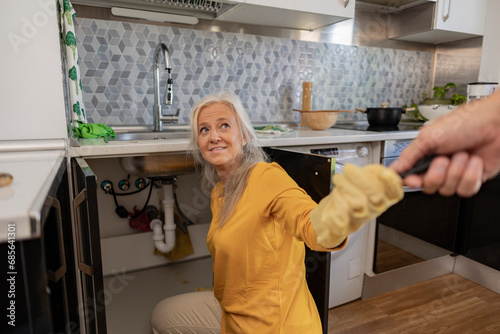 Mature woman doing plumbing in kitchen at home photo