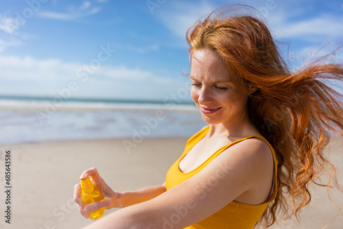 Smiling woman spraying suntan lotion on hand at beach