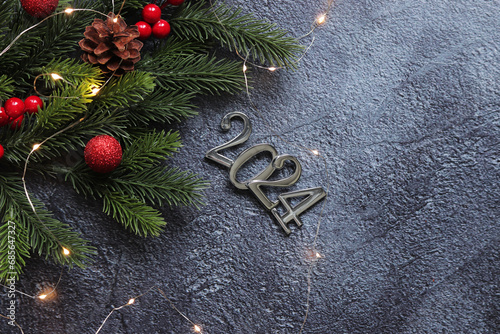 Happy New Year 2024, gray background with fir branch and Christmas balls and glowing garland on a gray background. New Year card, banner, top view, empty space. Christmas branch, silver numbers 2024