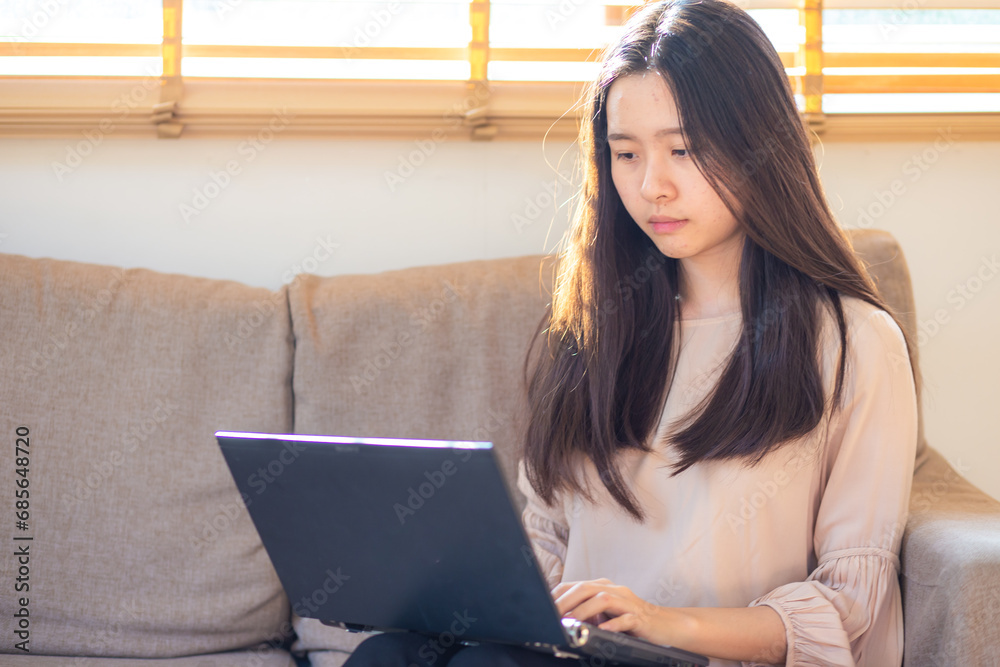 Business asian casual woman typing on laptop sitting on sofa in cozy home office Business asian casual woman typing on laptop sitting on sofa in cozy home office
