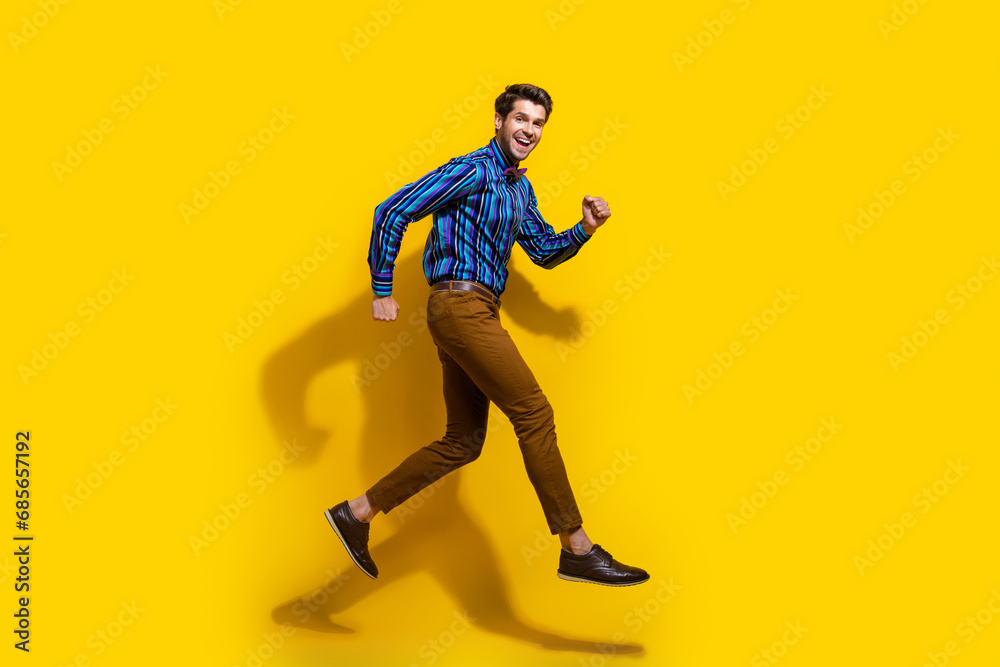 Full size photo of good mood guy dressed striped shirt brown trousers run shopping to empty space isolated on yellow color background