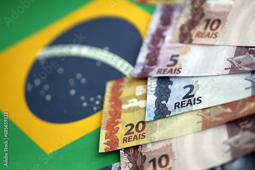 Brazilian money bills on top of the national flag of Federative Republic of Brazil close up