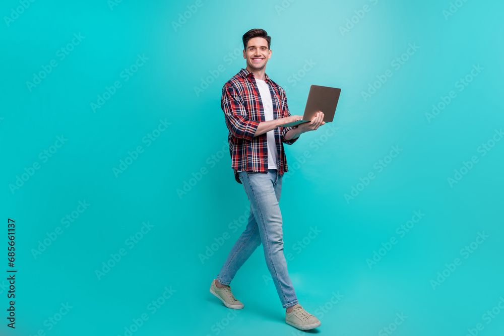 Full length photo of cool positive guy wear checkered shirt walking communicating modern device isolated teal color background