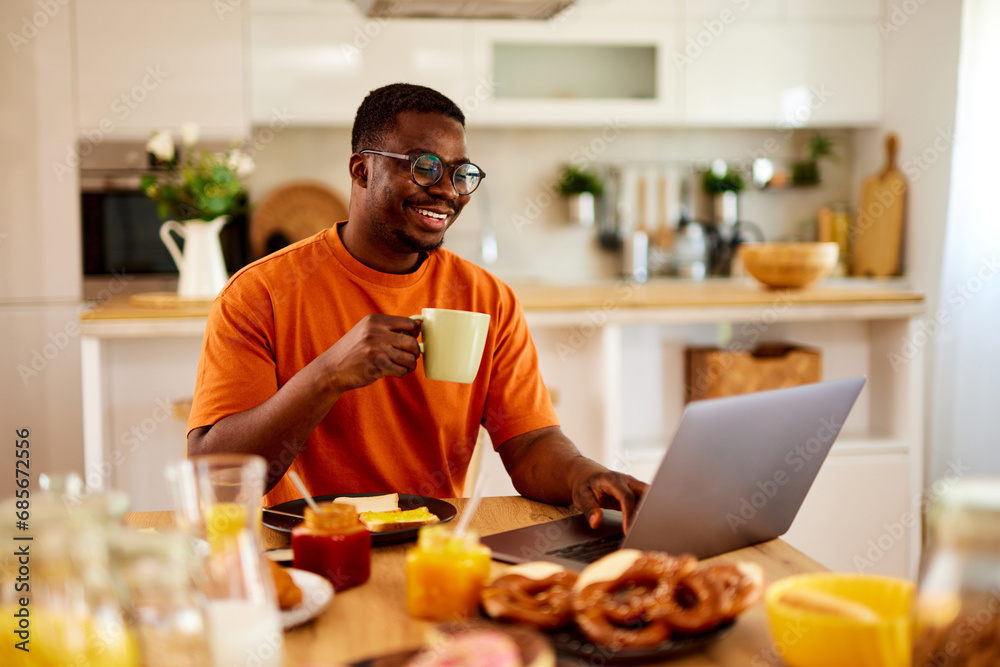 African American man using laptop while enjoying breakfast at home African American man using laptop while enjoying breakfast at home