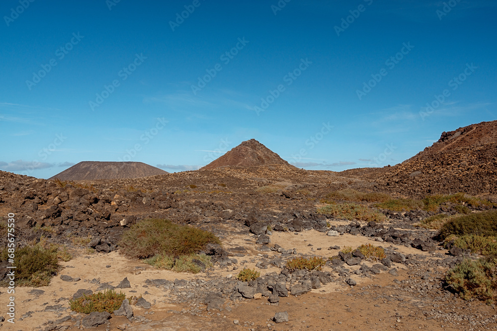 Lavahügel mit Sand und Lavasteinen im Vordergrund auf Fuerteventura